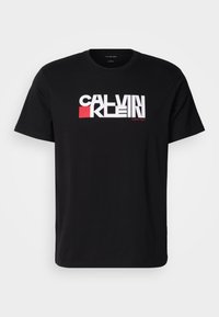 Fekete pamut póló, amelyen merész fehér és piros "CALVIN KLEIN" logó található a mellrészen. Rövid ujjak és környak kialakítás.