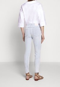 Jeans ajustados de color azul claro hechos de denim, combinados con una blusa de satén blanca de mangas cortas y sandalias marrones con tiras.