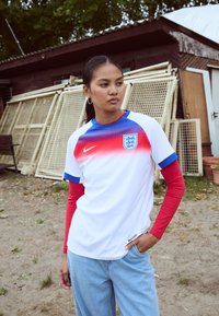 Balts futbola krekls ar sarkaniem un ziliem akcentiem, apaļš kakls un Anglijas emblēma. Valkāts virs sarkanas garām piedurknēm kreklu ar ziliem uzmava galiem.
