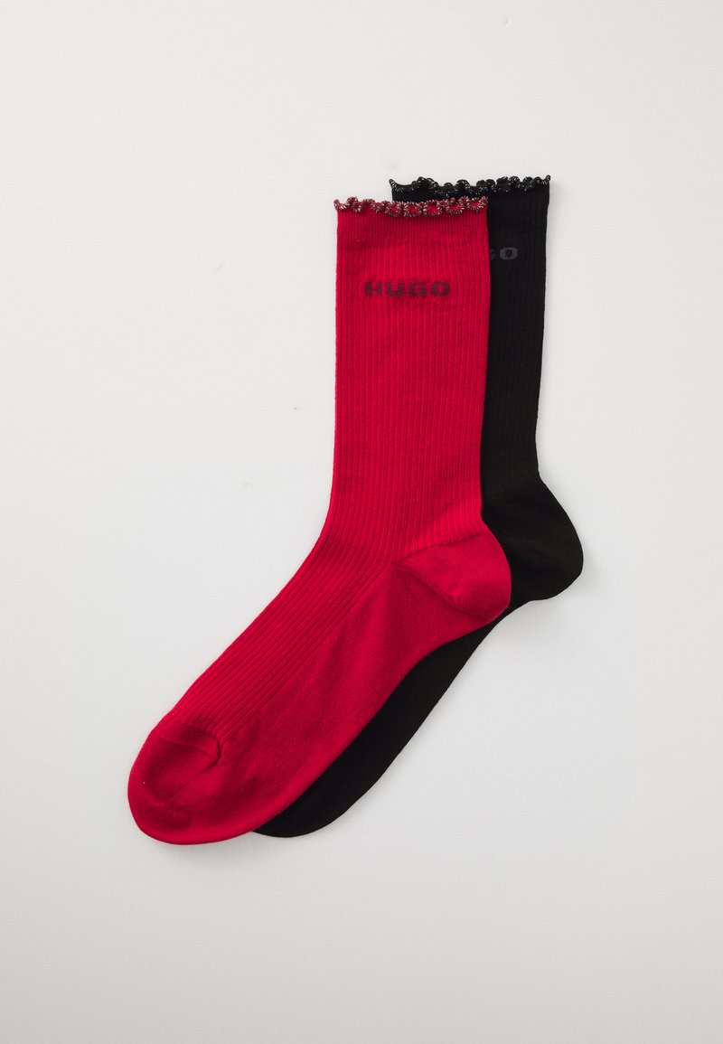 Par de calcetines acanalados, uno rojo y uno negro, con bordes fruncidos y el logo "HUGO" cerca del puño, dispuestos sobre un fondo blanco.
