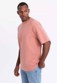 Světle růžové bavlněné tričko s uvolněným střihom, krátkými rukávy a kulatým výstřihem. V kombinaci se světle modrými denimovými džínami. Hladká textura.