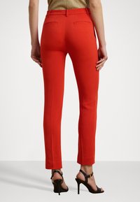 Rode strakke broek van soepel materiaal met een middelhoge tailleband, voorzien van twee achterzakken en een gestroomlijnd ontwerp. Gecombineerd met zwarte hakken.
