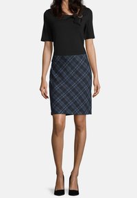 Svart topp med rosettdetalj, tillsammans med en marinblå rutad pennkjol. Slät tyg, figurnära silhuett, knälängd och stängd med en diskret midjeresår.