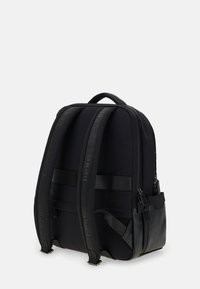 Svart ryggsäck tillverkad av ett slätt, hållbart material. Har vadderade axelremmar, flera fack och en stilren, minimalistisk design.