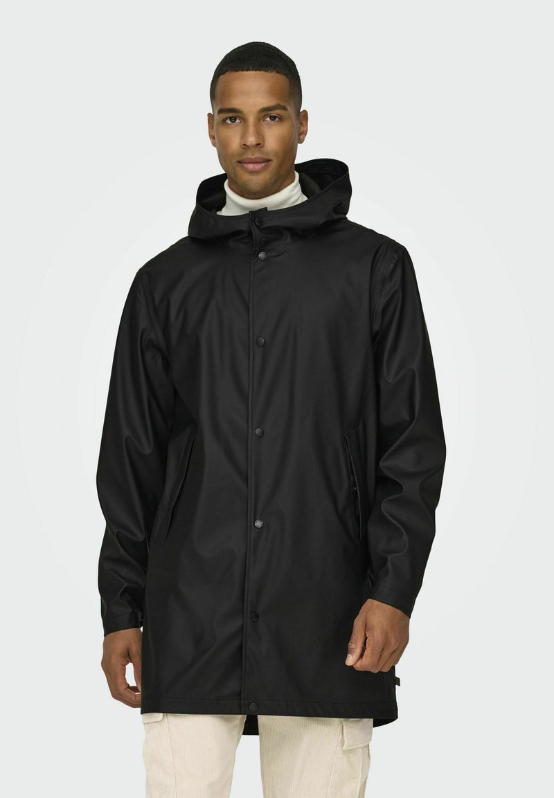 Chaqueta negra impermeable con capucha, adornada con botones a presión, bolsillos laterales y un acabado liso y brillante. Corte entallado.
