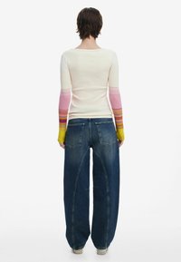 Rippstrick Langarmshirt mit pastellrosa und gelben Farbverlaufärmeln; hochgeschnittene, weite blaue Jeans mit Gesäßtaschen und Nähten.