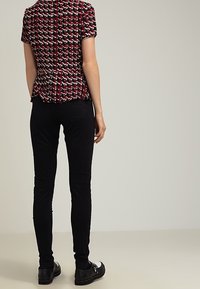 Bluzka z krótkim rękawem w czerwono-biało-czarny geometryczny wzór, w połączeniu z wąskimi czarnymi spodniami i butami z metalowymi akcentami.