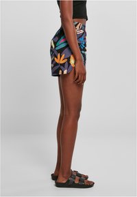 Shorts à motif floral bleu marine avec des accents vifs. Taille élastique, coupe ample. Sandales noires avec deux boucles.