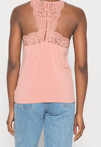 Rosa linne med spetsdetaljer på baksidan, med knappstängning. Mjuk tygkvalitet med en lös passform. Kombination med ljusblå denimjeans.