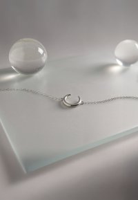 Silverarmband med ett halvmåneformat hängsmycke på en delikat kedja, visad på en frostad yta med glasorb.