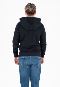 Felpa nera con cappuccio e tasca a marsupio, realizzata in cotone misto, con polsini e orlo a coste, indossata con jeans blu.