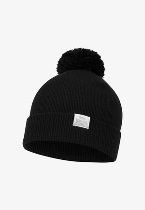 Bonnet en tricot noir avec une texture côtelée, doté d'un pompon noir duveteux sur le dessus et d'une étiquette de marque blanche à l'avant.