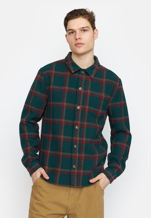 Groene en rode geruite flanellen shirt met een knoopsluiting aan de voorkant, spitse kraag en lange mouwen. Heeft een borstzak en bruine knopen.