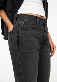 Jeans de mezclilla negra con un diseño ajustado, estilo de cinco bolsillos y una sutil textura desgastada. Cuenta con detalles de hardware en metal como botones y remaches.