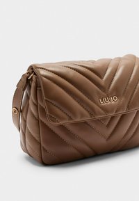 Braune gesteppten Lederhandtasche mit Klappenverschluss, diagonalem Nähten, goldfarbenen Beschlägen und einem dekorativen Logo auf der Vorderseite.