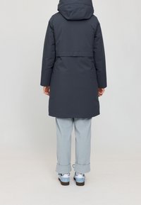 Manteau matelassé gris foncé avec capuche, taille cintrée par une ceinture, et manches longues. Associé à un pantalon bleu clair et des chaussures décontractées avec des accents bleus.