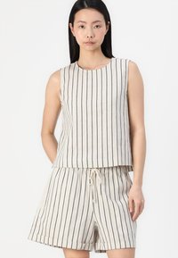 Bež potrgana tank top s mornarsko modrimi vertikalnimi črtami, v kombinaciji z ujemajočimi kratkimi hlačami. Top ima okroglo ovratnico; kratke hlače imajo elastičen pas.
