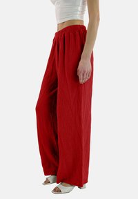 Rode, wijde broek gemaakt van textuurstof, met een elastische tailleband en een losse pasvorm. Gecombineerd met witte open-teenschoenen.