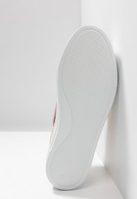 Semelle de chaussure présentant une surface en caoutchouc texturée, principalement blanche avec de légères rainures, et une forme courbée s'harmonisant avec une tige aux tons chauds.