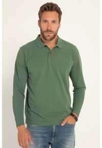 Langärmliges Poloshirt aus dunkelgrünem Stoff, mit klassischem Kragen, drei-Knopf-Leiste und tailliertem Schnitt. Getragen mit blauen Jeans.
