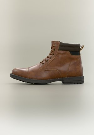 Bottine en cuir marron avec col matelassé noir, fermeture à lacets à l'avant et semelle en caoutchouc noire sur fond neutre.