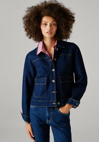 Σκούρα τζιν ζακέτα με κλείσιμο από κουμπιά, δύο μπροστινές τσέπες και αντίθετο ράψιμο. Διαθέτει ριγέ γιακά από κάτω.