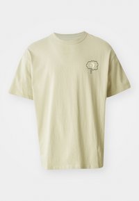 Light beige cotton t-shirt with short sleeves, featuring a small gray cloud graphic on the left chest area. Simple, boxy design.