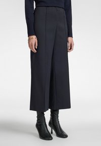 Navy wijde broek met een subtiele textuur, voorzien van een hoge taille en plooien. Gecombineerd met zwarte enkellaarsjes met hak.
