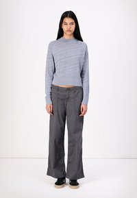 Pulover tricotat de culoare albastru deschis, cu un model texturat, asortat cu pantaloni gri largi și lejeri. Modelul poartă adidași negri.