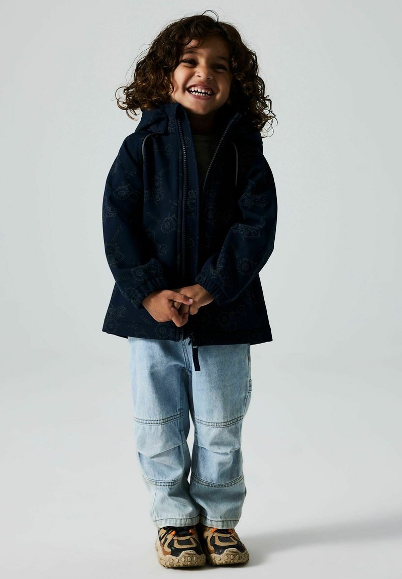 Veste navy avec capuche, texture à motifs, fermeture éclair à l'avant, associée à un pantalon en denim bleu clair et des baskets multicolores.