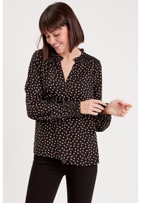 Black blouse with beige polka dots, buttoned neckline, long sleeves with gathered cuffs, and a relaxed fit. Textured fabric with a smooth finish.