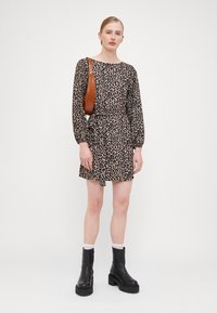 Leopardmønstret kjole i beige og sort, med lange ærmer og en samlet talje, parret med sorte kraftige støvler og en brun skuldertaske.