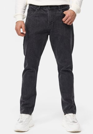 Black denim jeans with a relaxed fit, featuring five pockets, belt loops, and a faded finish. Worn with white sneakers.