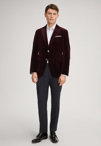 Bordeauxfarbener Samtblazer mit subtilen Mustern, zwei silbernen Knöpfen, Seitentaschen und Reverskragen; kombiniert mit dunklen Hosen und schwarzen Schuhen.