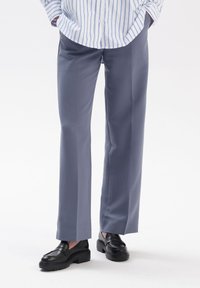 Dopasowane szare spodnie wykonane z gładkiego materiału, charakteryzujące się prostą nogawką i zgięciem z przodu, zestawione z czarnymi lofersami.