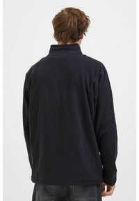 Pull-over en polaire navy avec un col haute, présentant une surface texturée et des manches longues. Le design comprend une coupe décontractée et un ourlet droit.