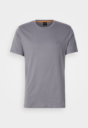 T-shirt gris à manches courtes en coton, avec un col rond et un petit écusson rectangulaire sur le côté supérieur gauche. Texture lisse.