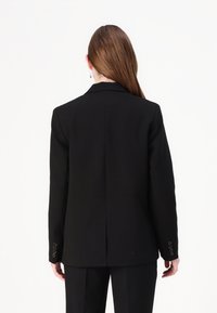 Čierny blazer so štruktúrovaným dizajnom, s výstrihom do tvaru písmena V, s jedným rozventilovaním na chrbte a guľatými manžetami. Ušité z kvalitného materiálu s hladkou textúrou.