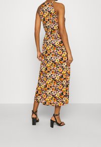 Vestido largo de flores con un fondo negro y patrones florales vibrantes en rosa, naranja y amarillo. Incluye un escote halter y un corte relajado.