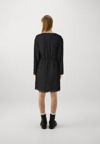 Μαύρο φόρεμα με μακριά μανίκια και ελαστική μέση, με υφή λουλουδιών και μήκος μέχρι το γόνατο. Φορεμένο πάνω από μποτάκια.