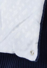 Tissu blanc avec un motif texturé chevauche un matériau côtelé bleu marine, comportant un détail de bouton-pression argenté sur le bord.