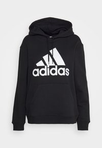 Sweatshirt à capuche noire en mélange de coton, arborant un grand logo Adidas blanc, une poche avant et des poignets élastiques. Design simple et décontracté.