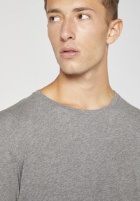 Grå crew neck t-shirt i mjukt, strukturerat tyg, med avslappnad passform och ribbad halsringning, delvis synlig på en models axel.