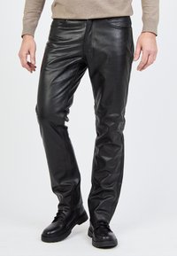 Schwarze Lederhosen in slimmer Passform mit Vorderseiten-Taschen und einer glatten Textur, kombiniert mit schwarzen Schnürstiefeln für einen Kontrast.