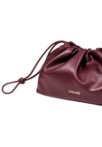 Bordeaux læder håndtaske med et samlet design, snorlukning og en detalje med guldlogo. Glat tekstur med en blød finish.