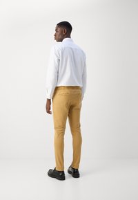 Chemise blanche à manches longues, pantalon jaune ajusté avec taille élastique et chaussures noires. Tissu lisse avec poches arrière et coupe ajustée.