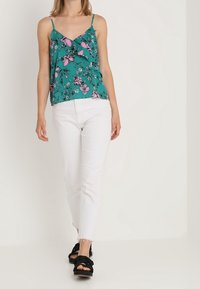 Turkusowy top na ramiączkach w kwiaty z falbaną z przodu, regulowane ramiączka, zestawiony z białymi krótkimi dżinsami i czarnymi sandałami z węzłem.