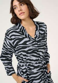 Abito a stampa zebra in nero e grigio, con scollatura a V e rifiniture arricciate, maniche lunghe e tasche. Realizzato in tessuto leggero.