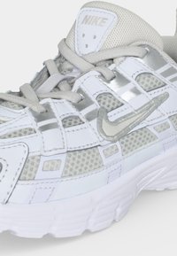 Witte en lichtgrijze Nike hardloopschoen met meshstof, synthetische overlays, veters en geborduurd Swoosh-logo aan de zijkant en op de tong.