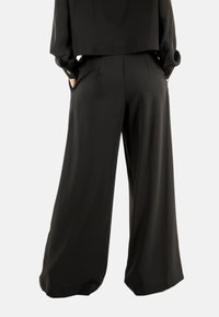 Pantaloni neri a gamba larga con una texture liscia, vita alta e tasche laterali, progettati per una vestibilità rilassata. Presentano un dettaglio plissettato sul fronte.